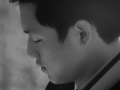 Black and white portrait of Kai Kim looking down and away from camera