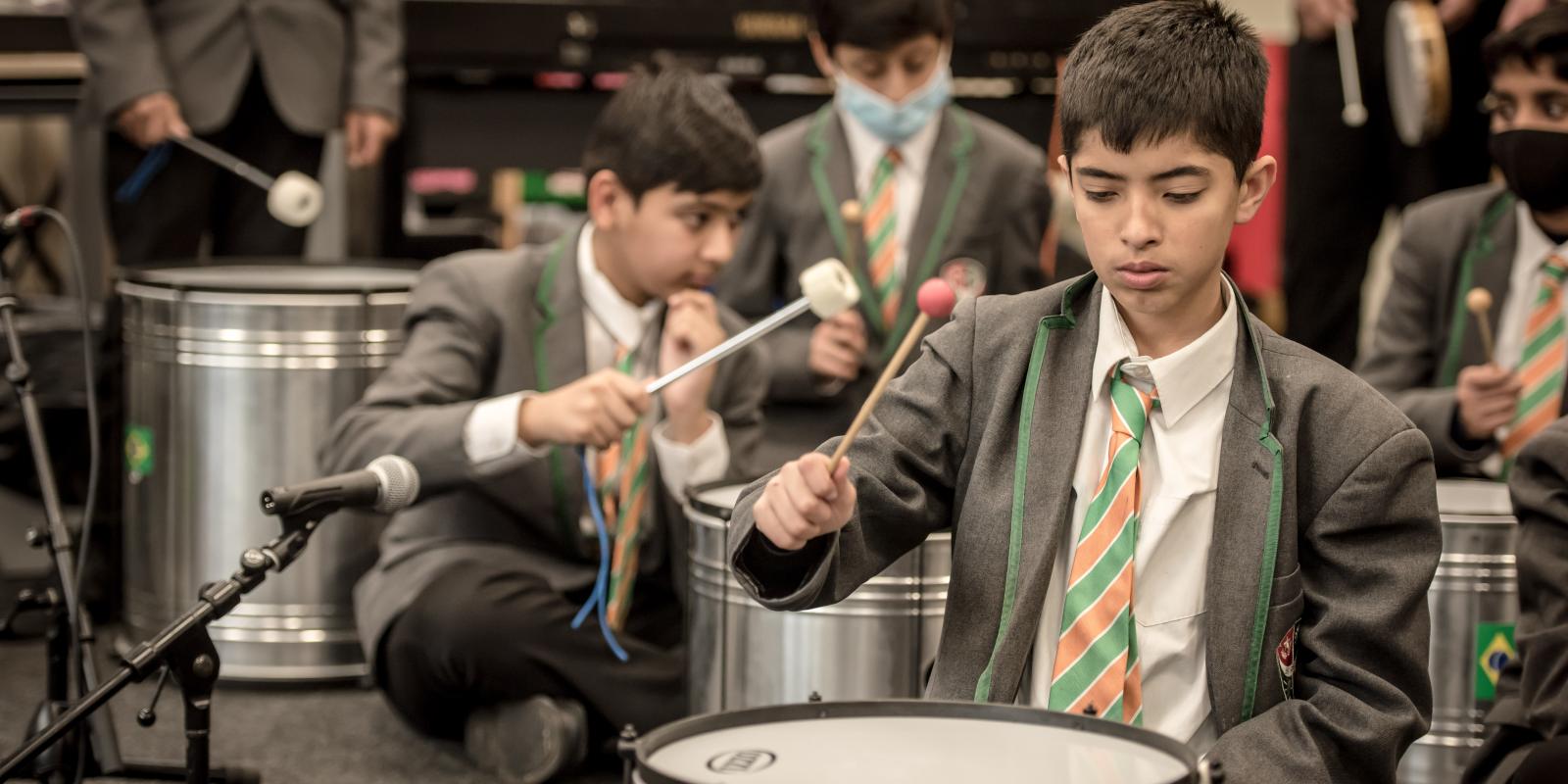 A pupil concentrates on striking a drum