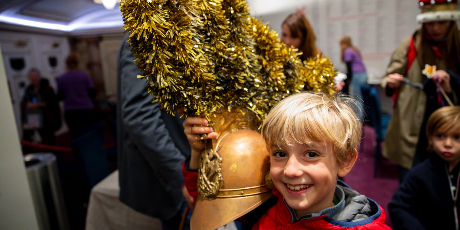 Young child proudly holding a soldier helmet taking part in costume dress up in the Stalls bar area of the London Coliseum during the interval of the Relaxed performance of ENO's Iolanthe---Wednesday 25 October 2023 © Lloyd Winters