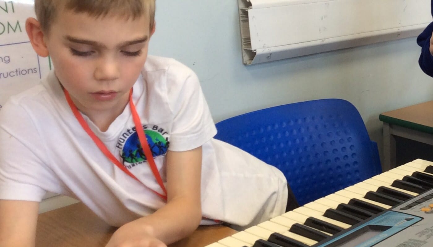 A pupil in white school uniform playing the keyboard